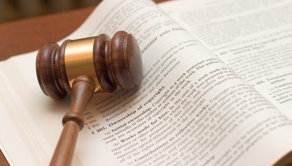 裁判で使う木槌(ガベル)が、著作権法の条文が書かれた法律書の上に置かれている様子。AIと著作権を巡る、法廷での攻防や司法判断を象実に徴する画像。